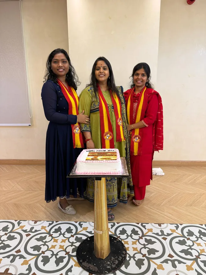 மகளிர் அணியைச் சேர்ந்த மூவர் கழக மேலாடையுடன் கேக்கின் பின்னால் நிற்கின்றனர்.